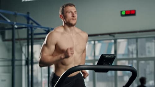 Shirtless Man Runs on Treadmill in Modern Gym