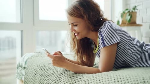 Happy Woman Using Smartphone Lying on Bed