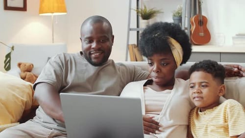 Positive Afro-American Family Using Laptop on Sofa and Posing for Camera