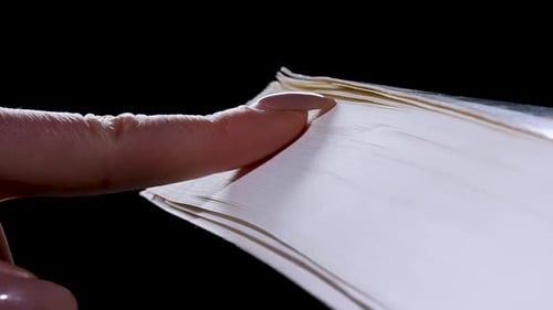The Girl Runs Her Fingernail Over the Pages of a Thick Book Flipping Through Them in Slow Motion