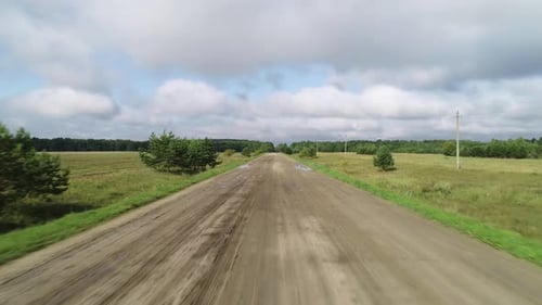 Flying Over a Dirt Rural Road Running Through Green Fields.