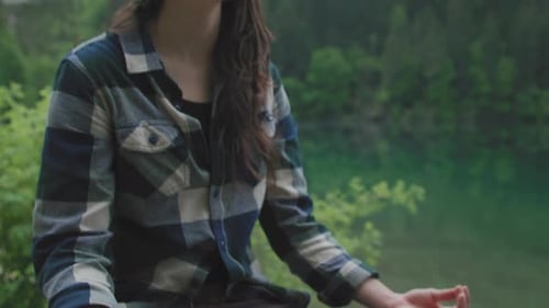 Handheld medium shot of a Woman doing Yoga and Meditation in a Lotus Pose on a rock above a beautifu