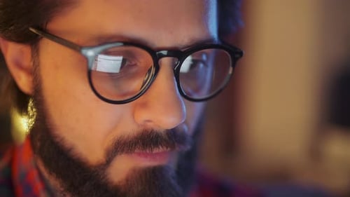 Nahaufnahme Porträt eines bärtigen jungen Geschäftsmannes mit Brille, der spät in seinem Büro sitzt