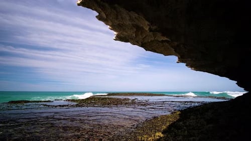 Small wave breaking on rocks on sunny day, shot from a cave, static shot