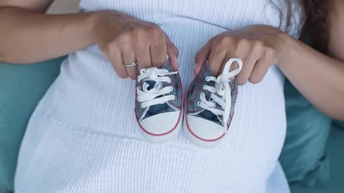 Expecting Woman Holds Baby Shoes Over Belly