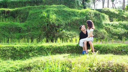 Young couple sitting in the middle of a lush green forest with the bright sun shining down on them