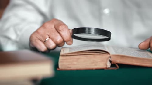 Gros plan, homme âgé, mains lisant un vieux livre de texte rétro, utilise une loupe pour rechercher des informations
