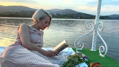 Una niña en una balsa lee un libro en medio del lago