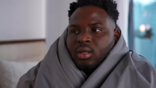 Portrait en gros plan d'un jeune homme malade avec de la fièvre couvert d'une couverture assis à l'intérieur