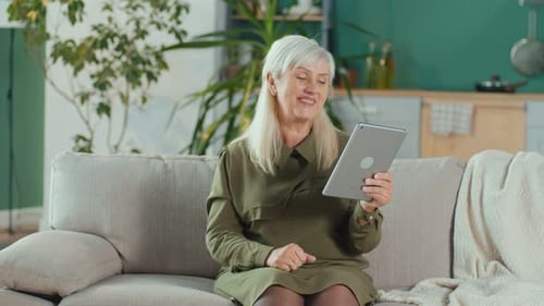 Senior Woman Using Tablet Device on Sofa at Home