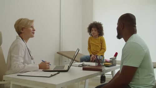 Doctor Consults With Child And Father In Medical Office