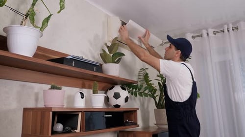 Male Handyman in Overalls Repairs or Cleans the Air Conditioner in the Apartment