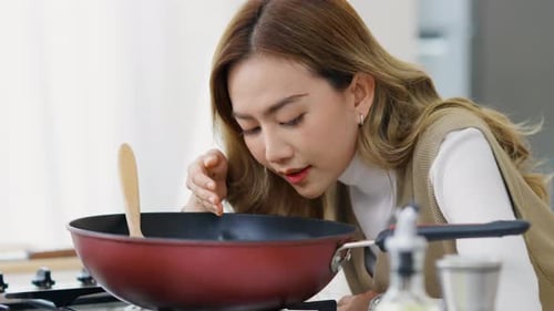 Woman Stirs Food in Frying Pan on Stove