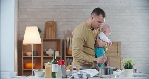 Father Holds Baby While Cooking in Kitchen