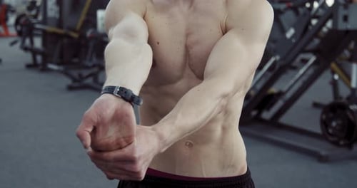 Shirtless Adult Stretching Wrists in Gym Setting