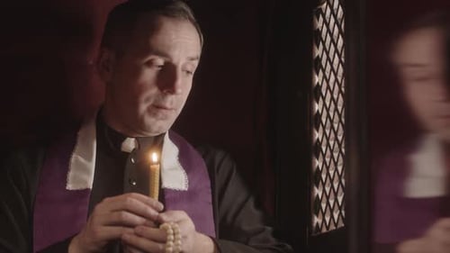 Priest with Candle Sitting in Confession Booth