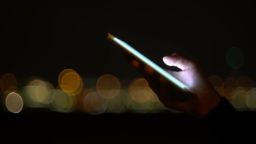 Hand Using Phone at Night with Bokeh Lights