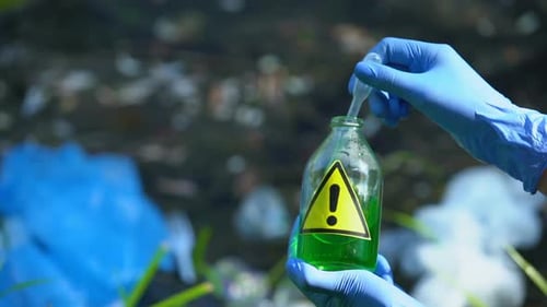 Ecologist Taking Liquid Sample From Bottle With Warning Sign, Polluted Area