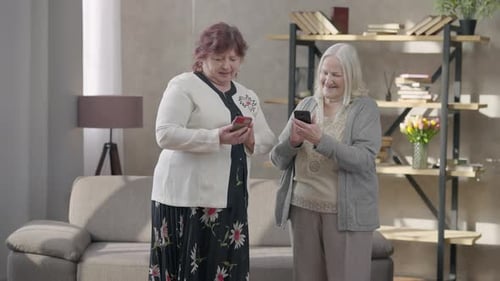 Two Senior Women Using Smartphones Together Indoors
