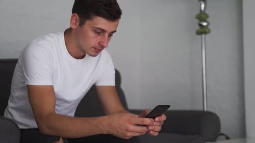 Young Man Using Smartphone on Gray Couch