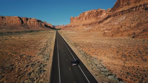 Drohnen-Kamera folgt silbernem Auto, das sich entlang der geraden Desert Highway Road zwischen erstaunlichen