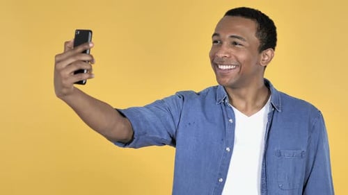 Young Adult Taking a Selfie with Phone on Yellow Background