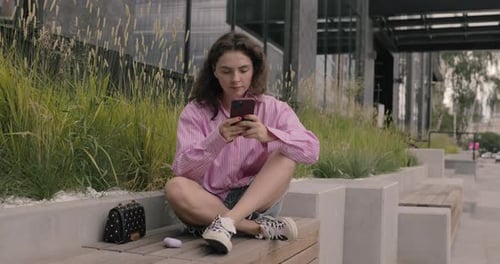Portrait of hipster woman typing by mobile phone on bus stop