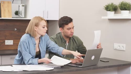 Couple Reviews Finances at Kitchen Table Using Laptop