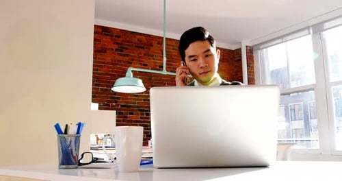 Young Adult Working on Laptop Answering Cell Phone