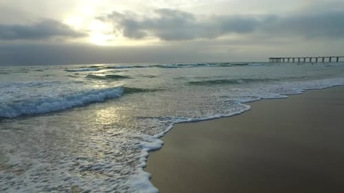 Tracking shot of the ocean waves, beach and pier at sunset.