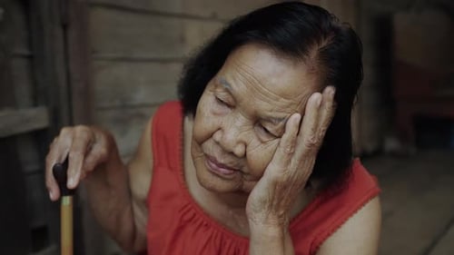 Thai elderly woman in round-necked sleeveless collar with headache and worried stressed face