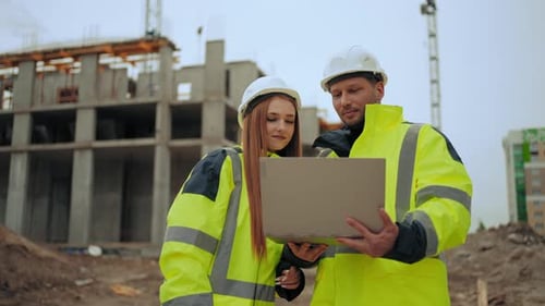 Two Civil Engineers are Discussing Project and Progress of Construction of Modern Building Outdoors