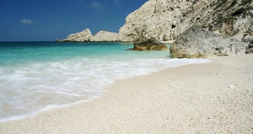 Clear Sea Waves Splashing on Peaceful White Beach with Pebbles Seascape with Rocks in Background