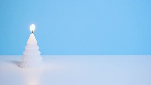 White Christmas Tree Wax Candle Burning on Blue Background