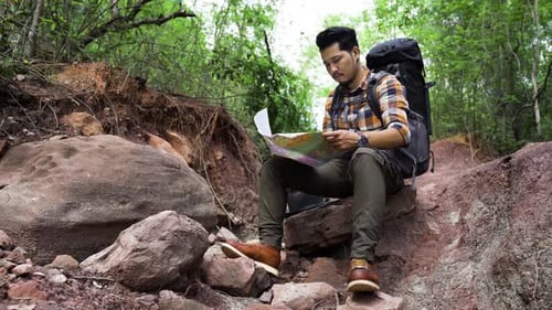 man traveler with backpack sitting and reading map in the natural forest