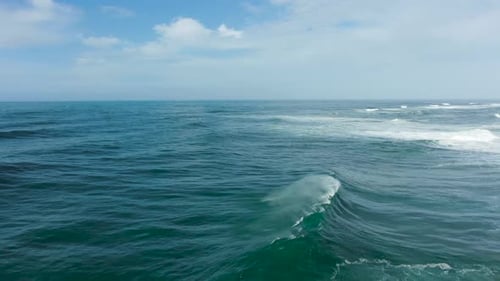 Large Waves Break on the Water Surface with Spray and Foam on a Sunny Day, Aerial View