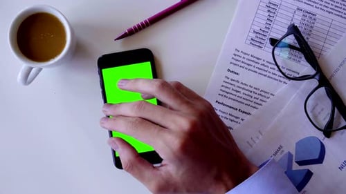 Man Using Smartphone Touch With Green Screen Chroma Key On White Office Table Background. Top View.