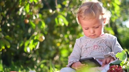 Little Child Uses Smartphone in Green Garden