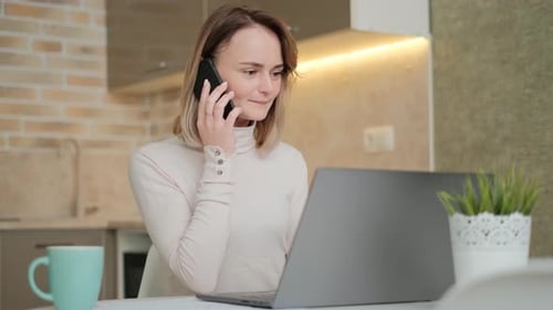 Woman Using Laptop Talking on Phone in Kitchen