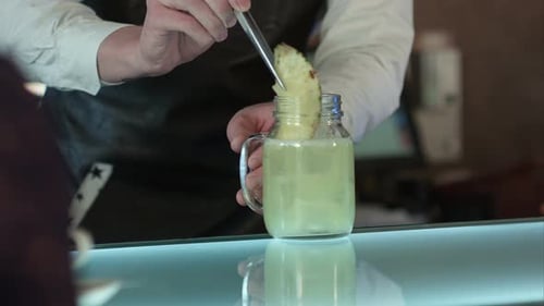 The Barman at the Bar Makes Cocktail with Ice, Decorating with a Piece of Pineapple