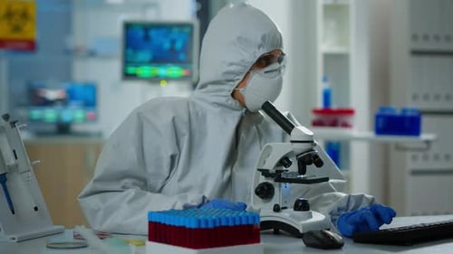 Scientist in Protective Suit Uses Microscope in Lab