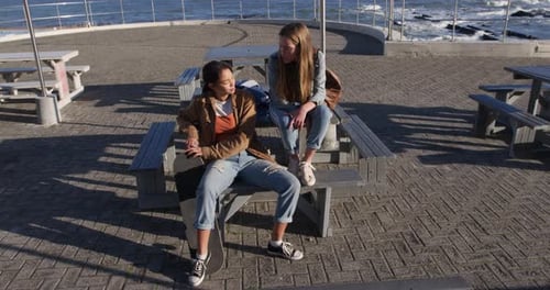 High angle view of a Caucasian and a mixed race girl talking sitting on a table