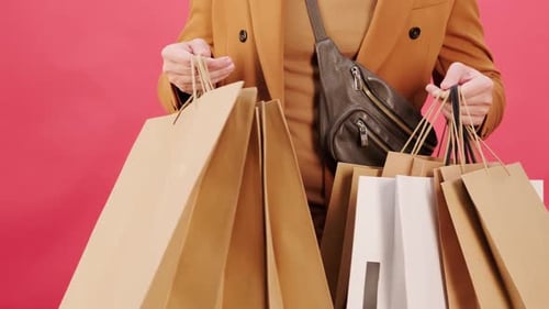 Person Holding Paper Shopping Bags on Pink Background