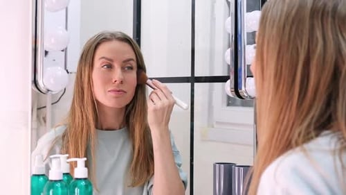 Woman Applies Makeup With Brush in Mirror
