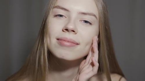 Close-up Beauty Portrait of Young Woman with Smooth Healthy Skin, She Gently Touches Her Face