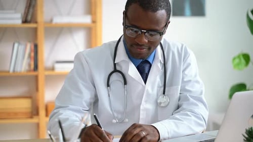 Young Male Doctor is Writing Report at Table with Laptop in Modern Clinic Spbas