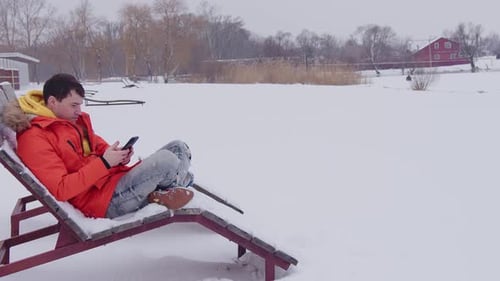 Young Adult Relaxing with Phone in Snowy Landscape