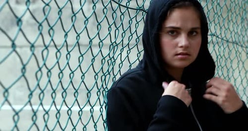 Portrait of sad schoolgirl in hooded leaning against fence