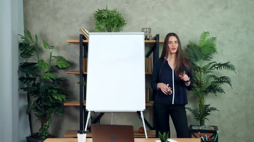 Woman Presenting Beside Whiteboard in Modern Office Setting