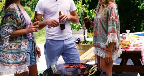 Group of friends having a bottle of beer while preparing barbeque